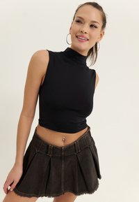 Must have mustaminekra crop top kõrge kaelusega, kombineerituna tume denimist plisseeritud seelikuga, millel on fatud äär ja vööaasad.