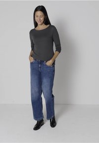 Gray long-sleeve top paired with loose-fit blue jeans. Model wears black ankle boots. Smooth texture, casual design, and classic blue denim.