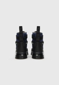 Bottines noires et marine avec un col rembourré, une semelle en caoutchouc et des sangles ajustables. Comprend des accentuations réfléchissantes et des tirettes.