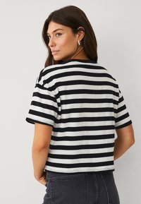 T-shirt cropped à rayures noir et blanc avec des manches courtes, un col rond et une texture en coton doux. La vue arrière montre des rayures horizontales.