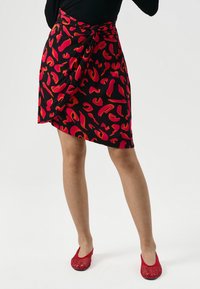 Gonna nera con vivaci motivi astratti rossi e arancioni, legata in vita, abbinata a scarpe slip-on in rete rosse.