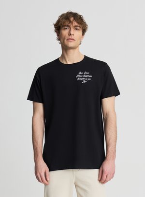 Uomo con capelli ricci che indossa una maglietta nera con testo bianco sul petto che recita "Love Beds Motel California Comfort as you Like."