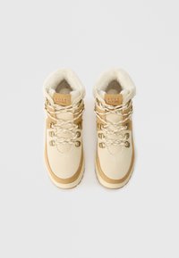 Αδιάβροχα μποτάκια πεζοπορίας σε μπεζ απόχρωση με καφέ λεπτομέρειες, διαθέτοντας επένδυση από ψεύτικη γούνάκι και μεταλλικά αξεσουάρ για πρόσθετη αντοχή και στυλ.