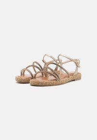 Strappy sandals featuring a metallic gold design with a braided jute sole and decorative rhinestone accents.