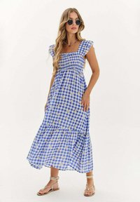 Modrá a biela kockovaná maxi šaty s puff rukávmi, zhmotneným telom a vrstvenou sukňou. Zlaté akcenty a vzorové detaily po celom oblečení.
