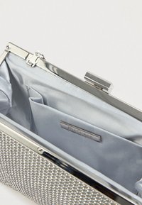 Kopertówka z kryształkami z metalową srebrną ramą, niebieską satynową wyściółką, z zapięciem na zatrzask, wewnętrzną kieszonką oraz metką marki. Kompaktowy i zorganizowany design.