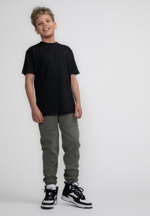 Zwarte katoenen T-shirt, olijfgroene joggingbroek met een gladde textuur, en zwart-witte sneakers met een hoge schacht.