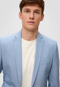 Blazer azzurro chiaro in tessuto texturizzato, chiusura con un solo bottone, revers a punta e taschino sul petto, indossato sopra una t-shirt bianca semplice.
