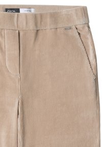 Beige corduroy broek close-up die de tailleband, de voorzak en het metalen merklabel aan de rechterkant toont.