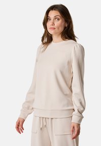 Felpa beige realizzata in morbido tessuto, con scollo rotondo, maniche lunghe a sbuffo e una vestibilità comoda, completata da polsini e orlo a coste.