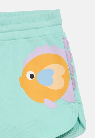 Shorts turquoise avec un poisson de dessin animé orange et violet aux nageoires bleues en forme de cœur imprimé près de la poche.