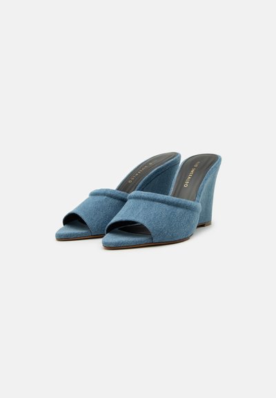 Muli wedge din denim albastru cu vârfuri deschise, o bandă lată în față și un finisaj din țesătură texturată. Tocul este unghiular și robust.