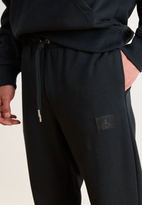 Sorte sweatpants med elastisk talje, snoretræk og sidelommer. Har et lille Jordan-logo i mørke nuancer på låret.