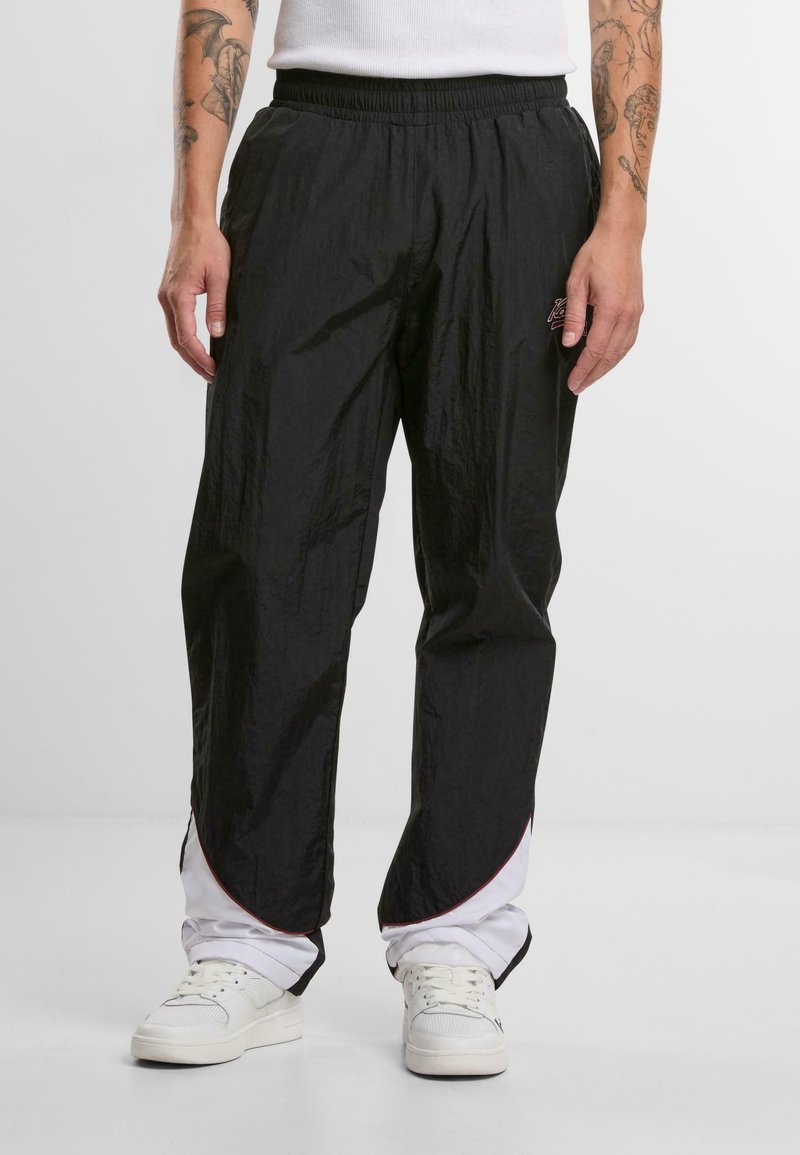 Pantalons légers noirs avec une taille élastique, présentant une surface texturée, des accents rouges le long de l'ourlet et des poches latérales.
