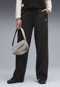 Black sweatpants with side pockets, paired with a light gray handbag featuring a curved design and textured finish. Black shoes.