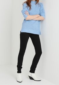 Maglione lavorato a maglia blu chiaro con una texture a coste, abbinato a jeans neri slim-fit e stivaletti bianchi alla caviglia con tacco a zeppa.