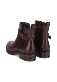 Brązowe skórzane botki za kostkę o gładkim wykończeniu, z bocznym zamkiem błyskawicznym oraz dekoracyjnym paskiem z okrągłą klamrą na cholewce. Niski, klinowy obcas.