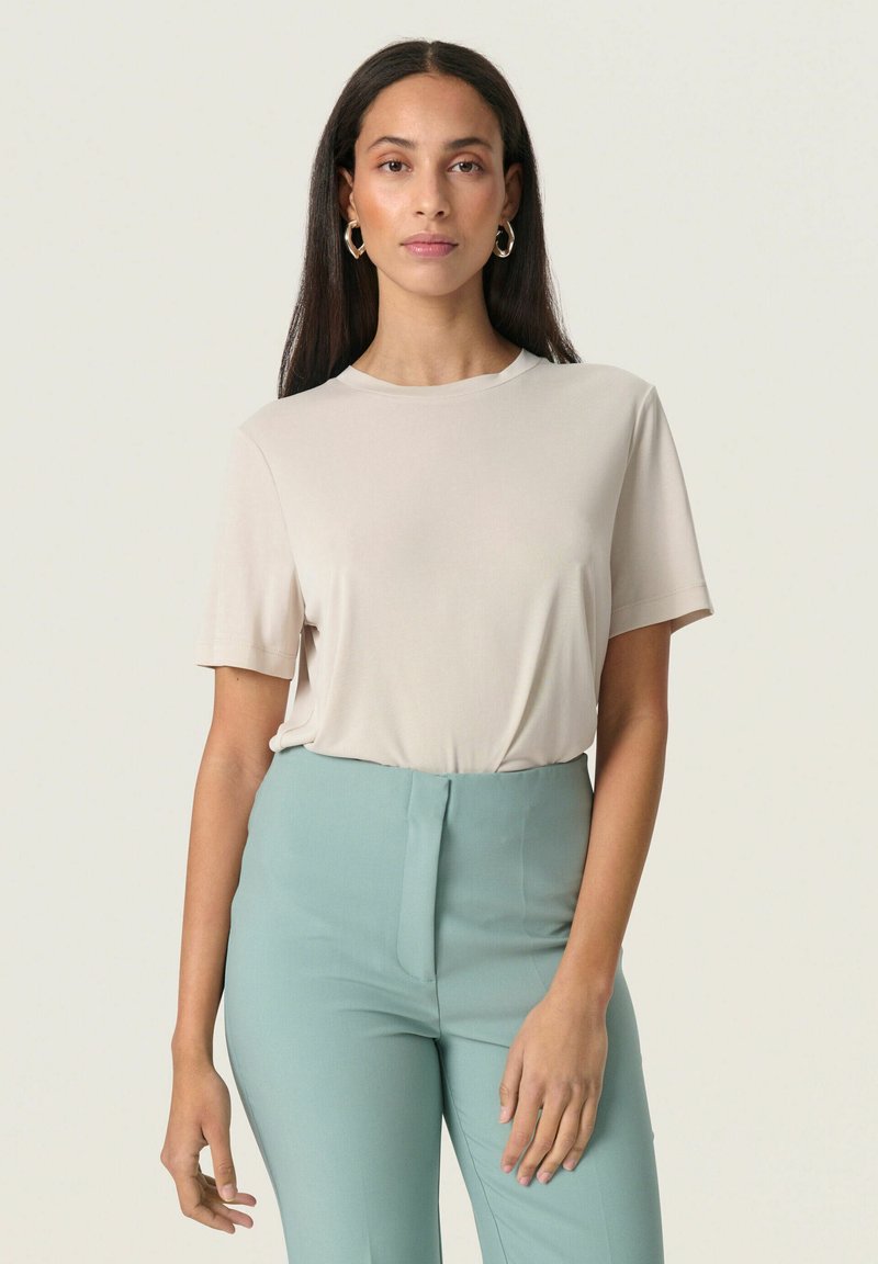 Beige kortærmet t-shirt med rund hals, glat tekstur, parret med lyst blå højtaljede bukser.