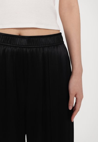 Pantalons en satin noir avec une coupe large, dotés d'une taille élastique. Le matériau présente une texture lisse et un subtil éclat.