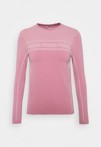 Růžový sportovní top s dlouhým rukávem a síťovanými panely, s nápisem "PUMA" přes hruď. Má hladkou látku a kontrastní švy.