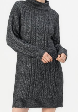 Robe-pull en maille torsadée gris foncé à manches longues et col montant, portée par une personne ajustant une manche.