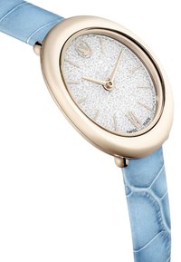Orologio tono oro con forma a goccia, quadrante glitter argento, indicatori delle ore beige e cinturino in pelle testurizzata azzurro chiaro.