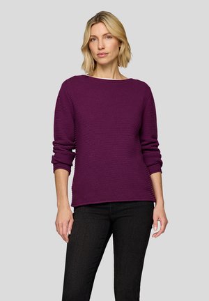 Lila gerippter Strickpullover mit weitem Ausschnitt und langen Ärmeln, kombiniert mit dunklen Jeans. Weiche Textur und lockere Passform.