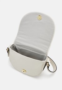 Bolso cruzado de piel beige con forma redondeada, herrajes dorados y un interior de tela gris. El cierre cuenta con un botón a presión para un ajuste seguro.