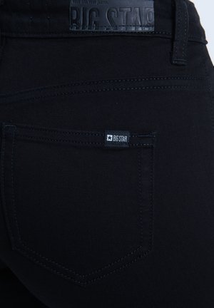 Mustad denim püksid, millel on sile tekstuur, nahast vöölipik ja väike kangast silt "BIG STAR" tagakotil.