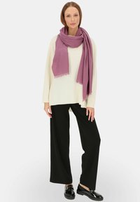 Jasnofioletowy szalik układa się na białym swetrze i czarnych szerokich spodniach; strój charakteryzuje się luźnym krojem z teksturowanym wykończeniem.