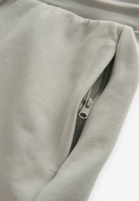Pantalones jogger gris claro hechos de una tela suave, con un bolsillo con cremallera y herrajes de cremallera a juego, y detalles de costura sutiles.