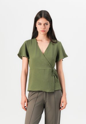Top în nuanță de verde măsliniu, cu mâneci scurte și vaporoase, fabricat dintr-un material texturat, și cu un detaliu legat la talie. Asortat cu pantaloni verzi măslinii.
