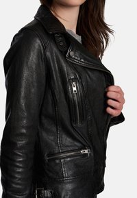 Svart bikerjacka i läder med inskuren krage, asymmetrisk frontdragkedja och flera dragkedjeförsedda fickor. Texturerad ytdetalj synlig.