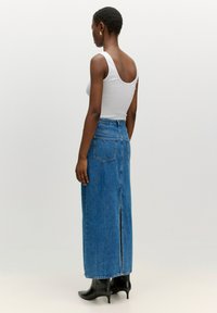 High-waisted denim rok in medium blauw met een achterkant split, met twee achterzakken en een gladde textuur. Gecombineerd met een witte tanktop.