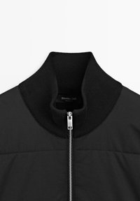 Giacca bomber nera con colletto alto a coste, chiusura frontale con cerniera e tessuto dalla texture liscia. Etichetta con la scritta "Massimo Dutti."