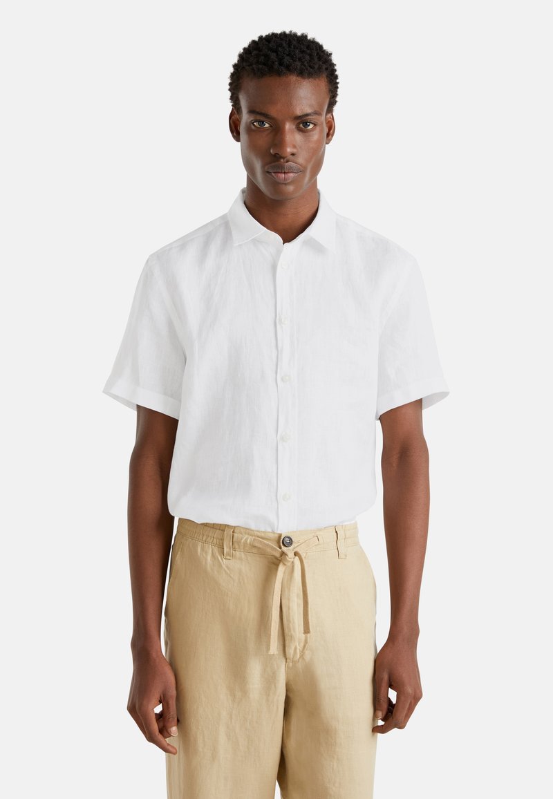 Camicetta bianca a maniche corte in lino con colletto alla francese e una leggera trama, abbinata a pantaloni beige con elastico in vita e bottone.