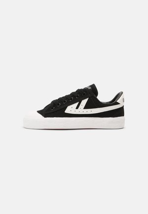 Black canvas sneakers with white rubber toe cap and sole, featuring a white side stripe and black laces. Textured outsole with wave pattern.