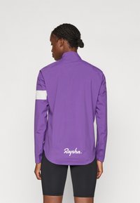 Paarse lichtgewicht jas van ademend materiaal met een hoge kraag, lange mouwen, een witte accentstreep en een logo aan de onderkant.