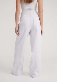 Pantaloni sweat grigi chiari a gamba larga realizzati in tessuto morbido. Presentano una vita elasticizzata e due tasche posteriori. Tessuto liscio e design casual.