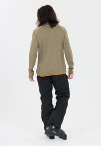 Åtsittande, beige långärmad topp med orange inslag, ihop med lösa svarta byxor och svarta skidboots, som visar en strukturerad tygdesign.