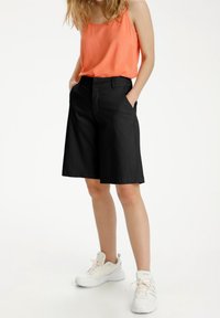 Black cotton shorts with a straight cut, featuring side pockets and a smooth texture. Paired with a coral tank top and white sneakers.