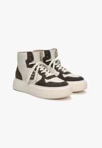 Vysoké tenisky s bílou koženou vrchní částí a hnědými zamíkovými akcenty, kulatou špičkou, silnou texturovanou podrážkou a kontrastním designem tkaniček.