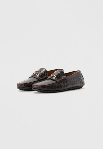 Mörkbruna loafers i läder med krokodilsmönster, detaljer i guldton, rund tå och strukturerad gummisul, visade sida vid sida.