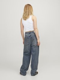 Jeans denim biru dengan potongan tinggi dan longgar, dengan pencucian yang pudar. Dilengkapi dengan dua kantong belakang dan loop sabuk. Dipadukan dengan atasan tank top putih.