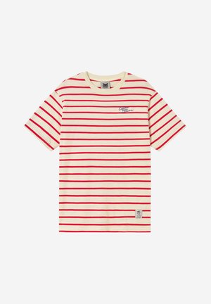 Κρεμ κοντομάνικη μπλούζα με κόκκινες οριζόντιες ρίγες, μικρό μπλε καλλιγραφικό κείμενο στο στήθος και ορθογώνιο αυτοκόλλητο κοντά στο κάτω τελείωμα.