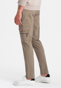 Pantaloni cargo beige con tasche laterali, dettaglio con zip, taglio dritto e un tessuto liscio e leggero. Abbinati a sneaker bianche.