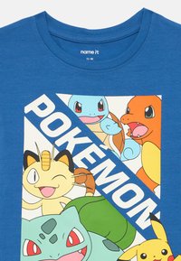 Modré bavlnené tričko s farebnou grafikou Pokémonov, vrátane postáv ako Squirtle, Charmander, Meowth, Bulbasaur a Pikachu.