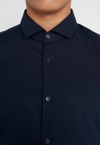Camisa de botones azul marino con cuello extendido, hecha de una tela suave, con botones negros y un diseño frontal limpio.