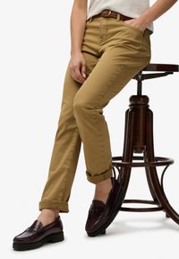 Pantalones de corte slim en color caqui con puños enrollados, hechos de algodón suave, combinados con mocasines burdeos que presentan una superficie y suela texturizadas.