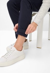 Marineblaue Stretchhosen mit umgeschlagenem Saum, kombiniert mit weißen Ledersneakers mit dicker Sohle und auffälligen Steppdetails.